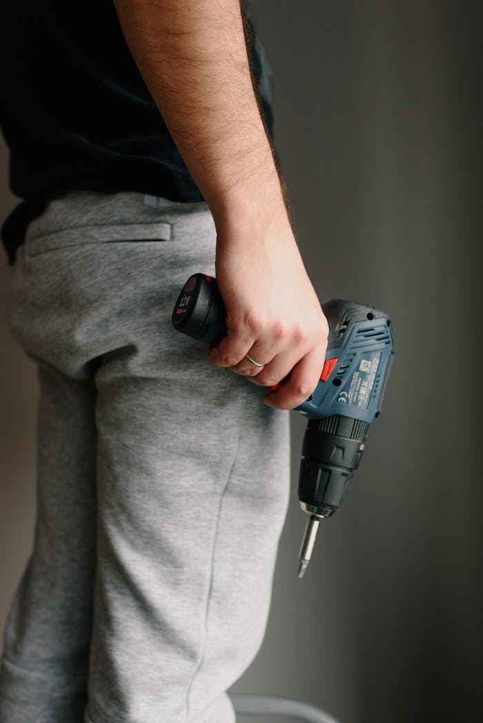 A man holds a cordless drill, ready for work, against a neutral indoor background.